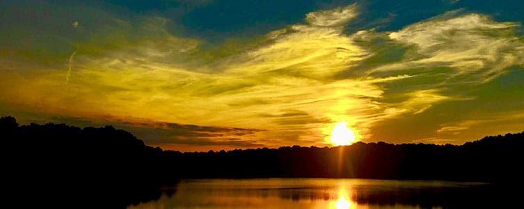 sun setting over lake and trees