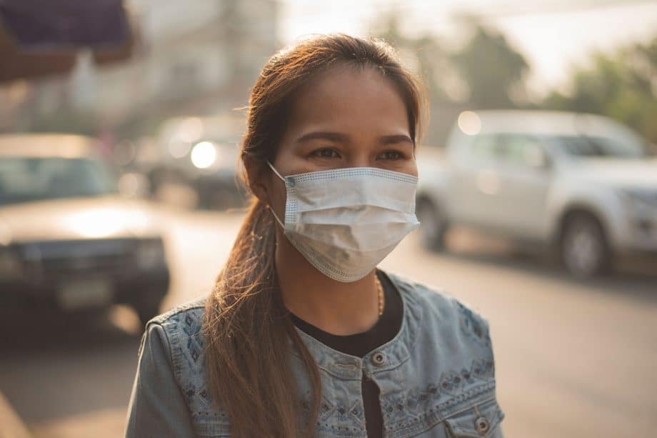 woman walking on sidewalk with hair in ponytail wearing a surgical mask